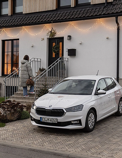 Das Bild zeigt eine Hebamme der Praxis Meilenstein während eines Hausbesuchs in Neuhausen auf den Fildern. Im Vordergrund steht ein weißes Auto in der gepflasterten Einfahrt eines modernen Einfamilienhauses. Die Fassade des Hauses ist warm beleuchtet, und eine Frau geht die Treppe zum Eingang hoch – symbolisch für den persönlichen, einfühlsamen und individuellen Betreuungsansatz der Hebammenpraxis. Das Bild vermittelt eine ruhige, vertrauensvolle Atmosphäre und unterstreicht den Fokus der Praxis Meilenstein auf mobile Wochenbettbetreuung, Hausbesuche und persönliche Betreuung von Familien in Neuhausen auf den Fildern und der Region Filderstadt.