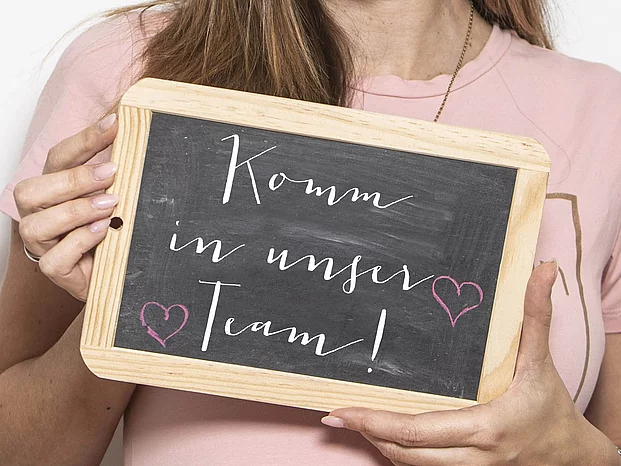 Frau hält Schild hoch, mit dem Text: Komm in unser Team