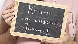 Hebamme hält Bild hoch mit der Aufschrift - komm in unser Team 